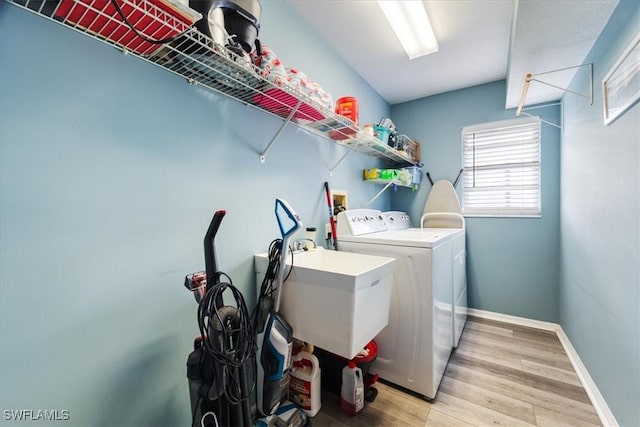 clothes washing area with washer and clothes dryer, sink, and hardwood / wood-style flooring