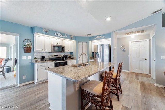 kitchen featuring light stone countertops, sink, stainless steel appliances, a kitchen bar, and white cabinets