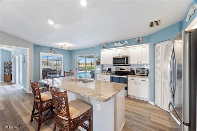 kitchen with a kitchen island with sink, white cabinets, sink, appliances with stainless steel finishes, and a breakfast bar area