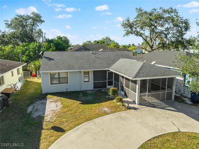 view of front of home with a shingled roof, concrete driveway, a front lawn, and a sunroom