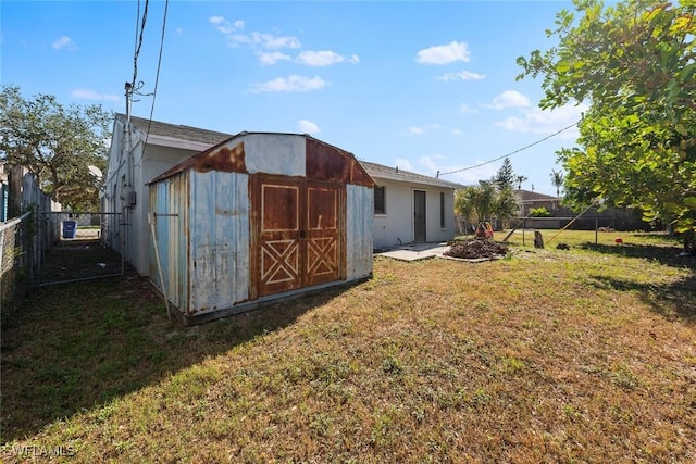 rear view of property featuring an outbuilding, a lawn, a storage unit, and fence