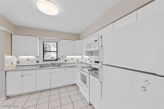 kitchen with white appliances, light stone counters, light tile patterned floors, a sink, and white cabinetry