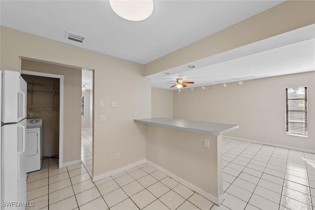 kitchen featuring light tile patterned floors, visible vents, washer / dryer, a peninsula, and freestanding refrigerator