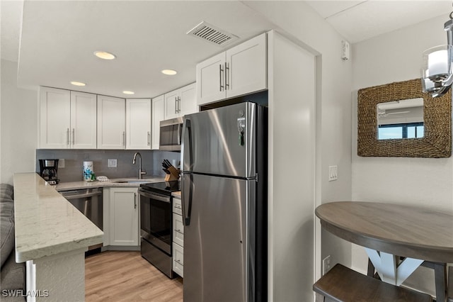 kitchen with sink, appliances with stainless steel finishes, light hardwood / wood-style floors, white cabinets, and kitchen peninsula