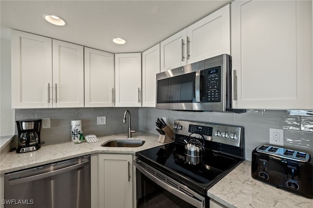 kitchen featuring sink, light stone counters, tasteful backsplash, stainless steel appliances, and white cabinets