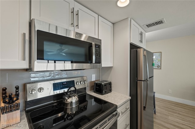 kitchen with white cabinets, decorative backsplash, light stone counters, stainless steel appliances, and light hardwood / wood-style flooring