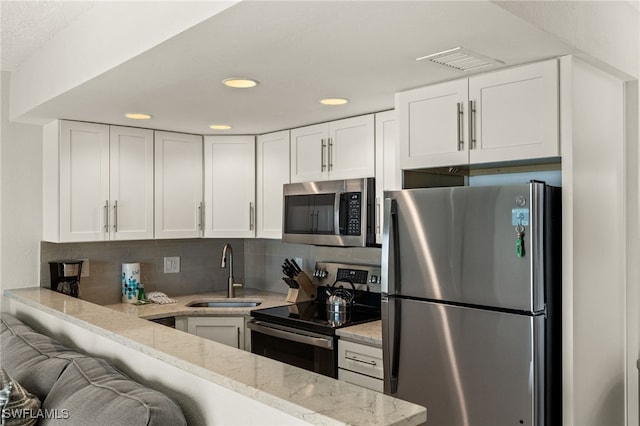 kitchen featuring stainless steel appliances, white cabinetry, light stone countertops, and sink