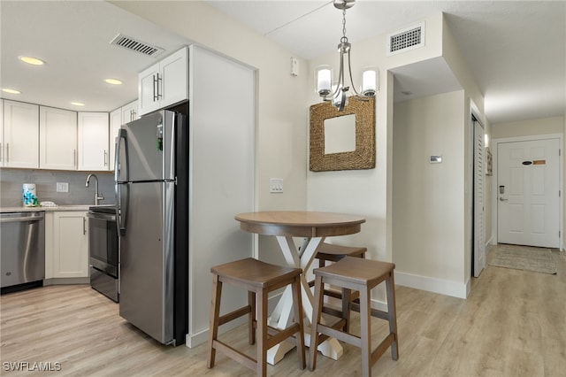 kitchen featuring white cabinetry, appliances with stainless steel finishes, light hardwood / wood-style floors, and pendant lighting