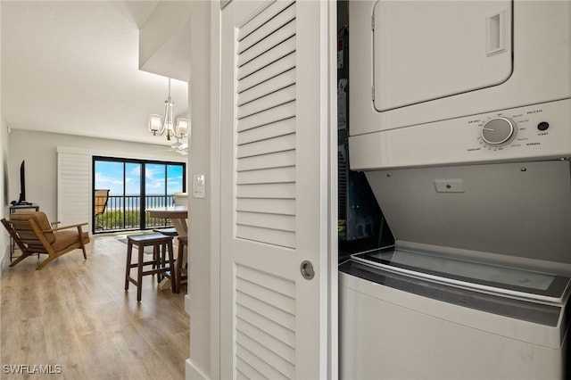 clothes washing area with stacked washer / drying machine, a notable chandelier, and light hardwood / wood-style floors