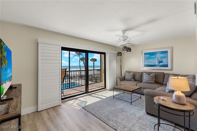 living room featuring light hardwood / wood-style flooring, ceiling fan, and a water view