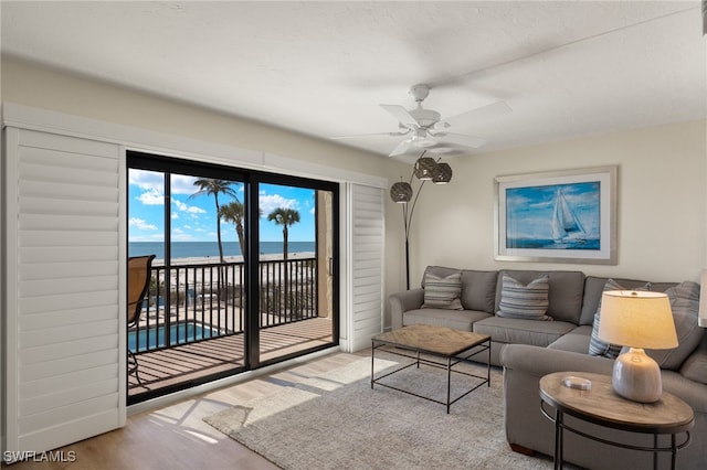 living room featuring light wood-type flooring, ceiling fan, and a water view