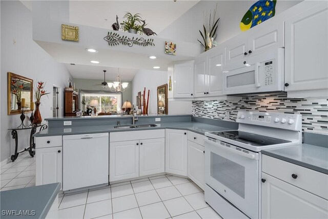 kitchen with kitchen peninsula, white appliances, vaulted ceiling, sink, and white cabinetry