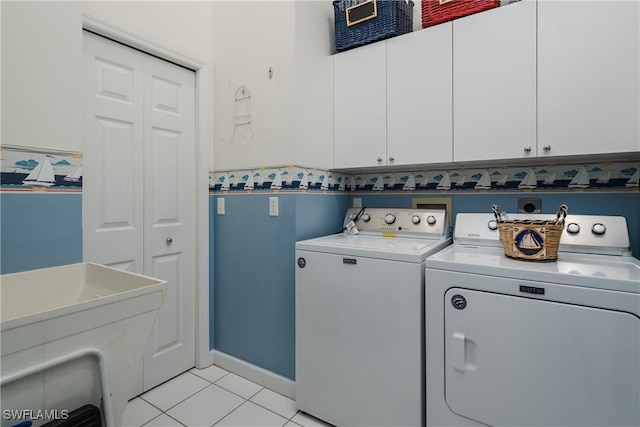 washroom featuring cabinet space, light tile patterned floors, baseboards, washer and dryer, and a sink