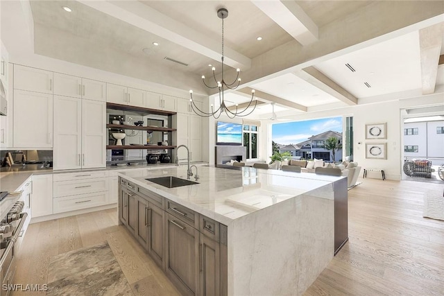 kitchen with light stone counters, a spacious island, sink, pendant lighting, and white cabinets