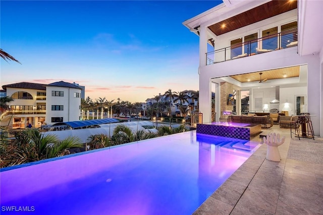 pool at dusk featuring outdoor lounge area, ceiling fan, and a patio area