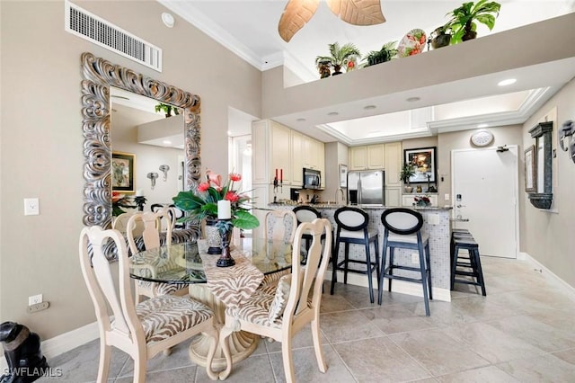 dining space with sink, a high ceiling, crown molding, a tray ceiling, and light tile patterned floors