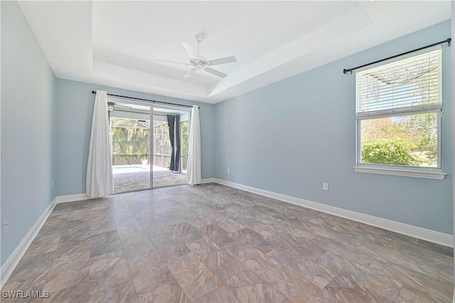 unfurnished room with a raised ceiling, ceiling fan, and a wealth of natural light