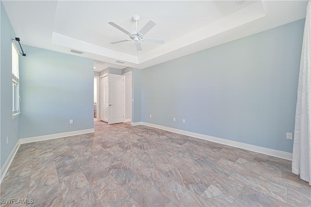 empty room featuring ceiling fan and a tray ceiling