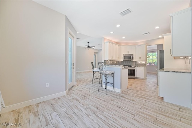 kitchen featuring appliances with stainless steel finishes, light wood-type flooring, a breakfast bar, light stone counters, and white cabinets