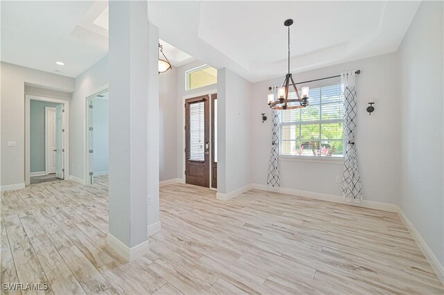 entryway with light hardwood / wood-style floors, a notable chandelier, and a raised ceiling