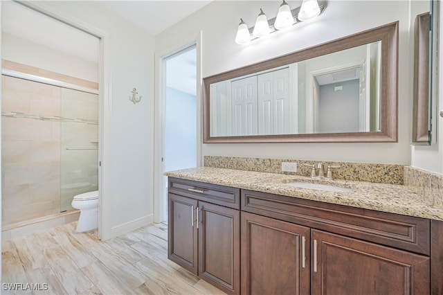 bathroom featuring a shower with door, vanity, and toilet