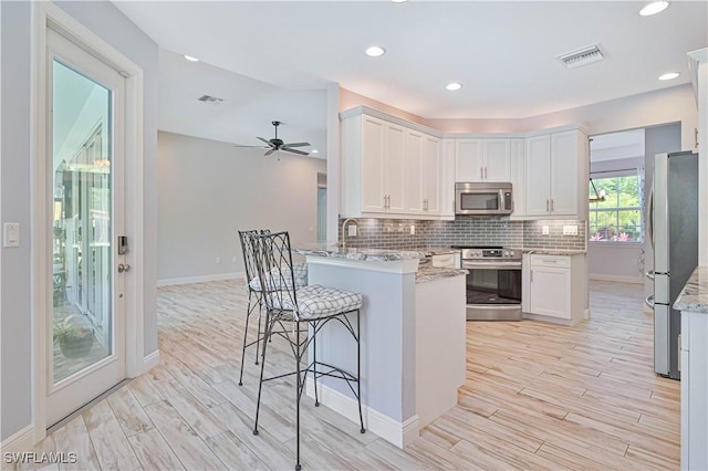 kitchen with appliances with stainless steel finishes, ceiling fan, white cabinetry, and kitchen peninsula