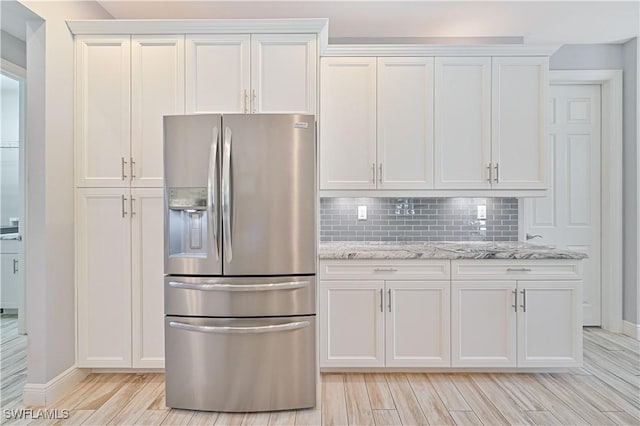 kitchen with stainless steel fridge with ice dispenser, white cabinetry, decorative backsplash, and light stone countertops