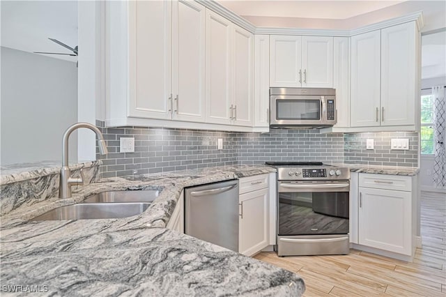 kitchen featuring light stone counters, stainless steel appliances, white cabinets, and sink