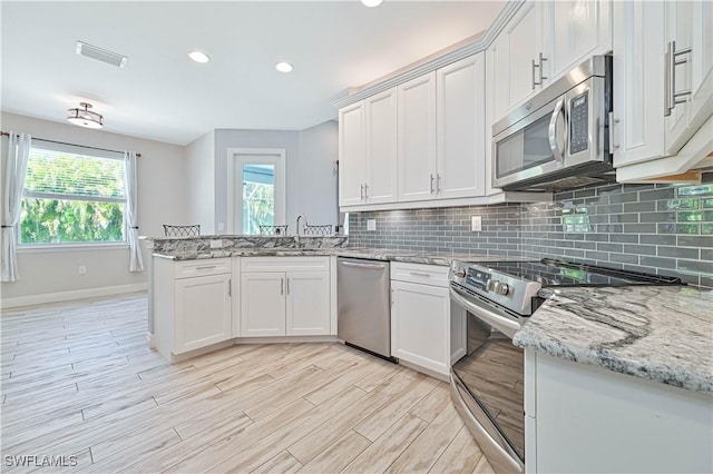 kitchen with stainless steel appliances, light stone countertops, and white cabinetry