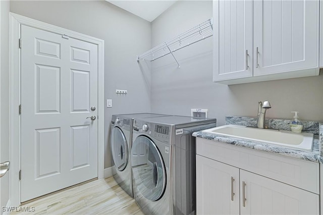 clothes washing area featuring sink, washing machine and dryer, and cabinets