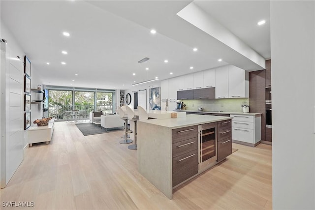 kitchen with light wood-type flooring, expansive windows, a spacious island, white cabinets, and wine cooler