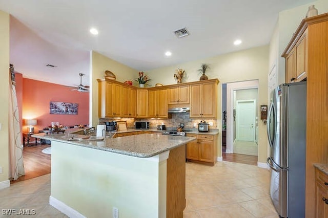 kitchen featuring light stone counters, ceiling fan, light tile patterned floors, kitchen peninsula, and stainless steel fridge