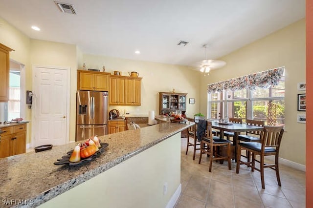 kitchen featuring stainless steel refrigerator with ice dispenser, light tile patterned floors, and light stone counters