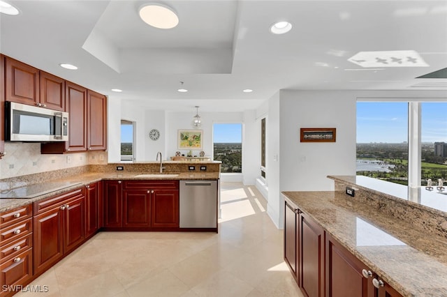 kitchen featuring appliances with stainless steel finishes, sink, backsplash, a tray ceiling, and light stone countertops