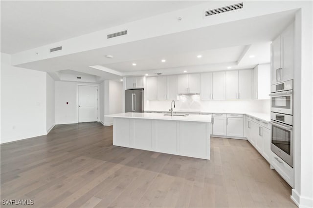 kitchen featuring a center island with sink, a raised ceiling, white cabinets, appliances with stainless steel finishes, and sink