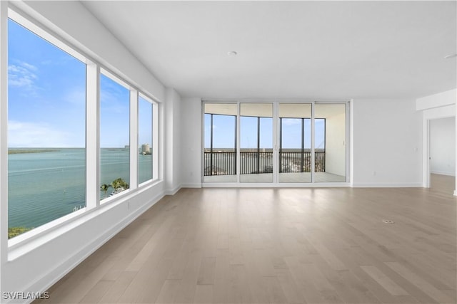 empty room featuring light wood-type flooring, a water view, and a wealth of natural light