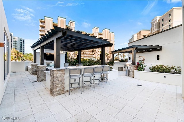 view of patio with exterior kitchen, a bar, and a pergola