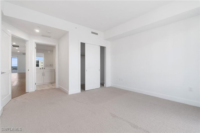 unfurnished bedroom with light colored carpet, a closet, and ensuite bath