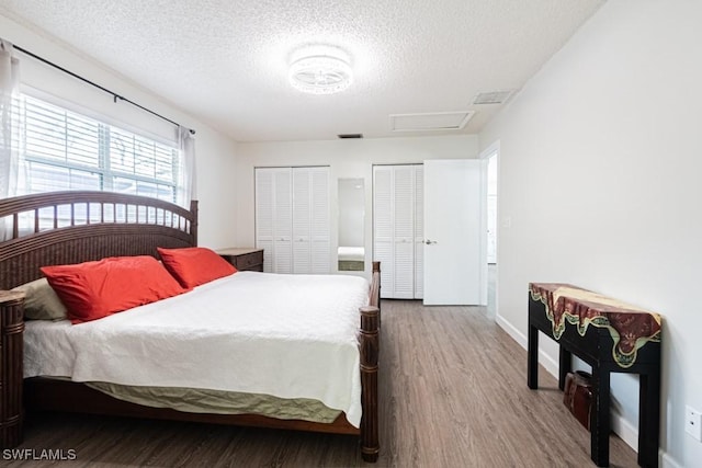 bedroom with wood-type flooring, two closets, and a textured ceiling