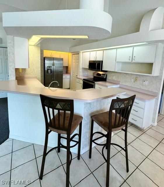 kitchen featuring kitchen peninsula, appliances with stainless steel finishes, white cabinetry, and a kitchen breakfast bar