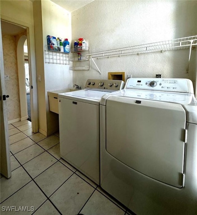 clothes washing area with sink, light tile patterned floors, and independent washer and dryer