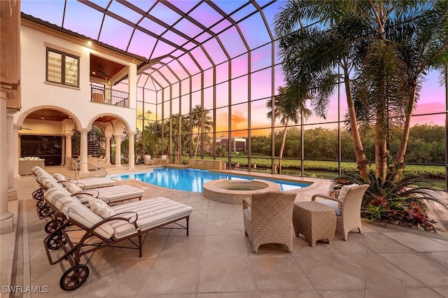 pool at dusk with glass enclosure, an in ground hot tub, and a patio