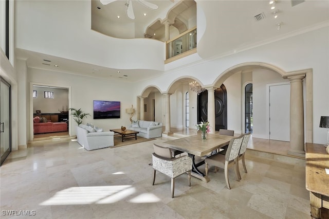 dining space with ornate columns, ceiling fan, crown molding, and a towering ceiling