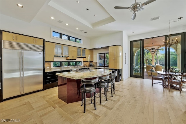 kitchen featuring stainless steel appliances, light stone counters, a breakfast bar, a kitchen island, and ceiling fan with notable chandelier