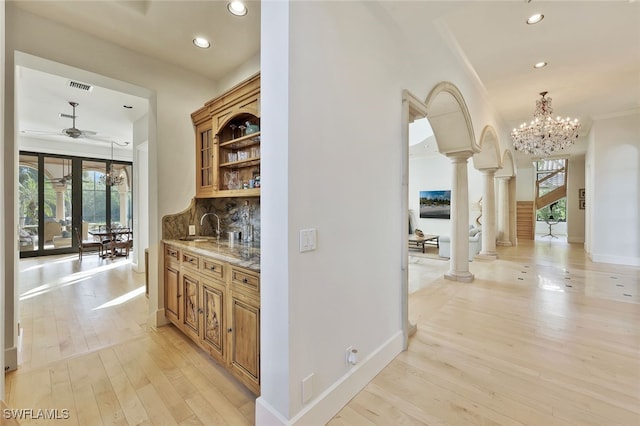 corridor with light hardwood / wood-style floors, a healthy amount of sunlight, ornate columns, and an inviting chandelier