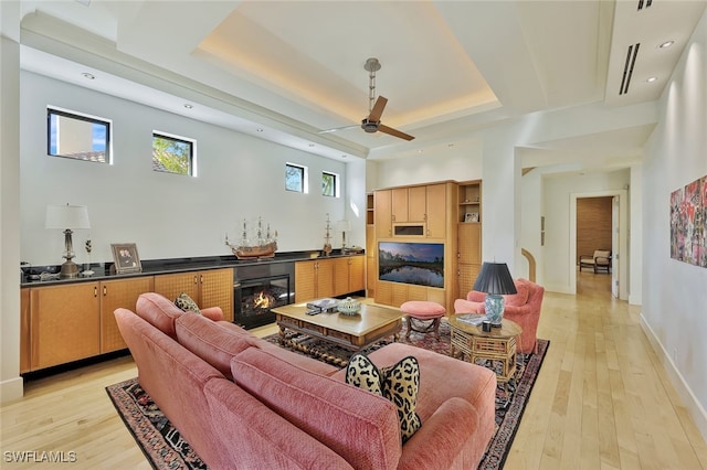 living room with light hardwood / wood-style flooring, a raised ceiling, and ceiling fan