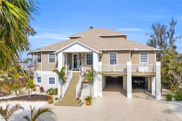 coastal inspired home featuring covered porch, a carport, a shingled roof, and concrete driveway