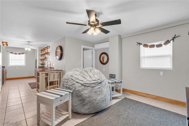 living area with light tile patterned floors, a wall mounted AC, a ceiling fan, and baseboards