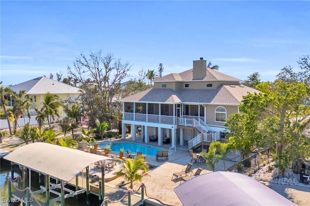 rear view of house featuring a patio, boat lift, a sunroom, stairway, and an outdoor pool