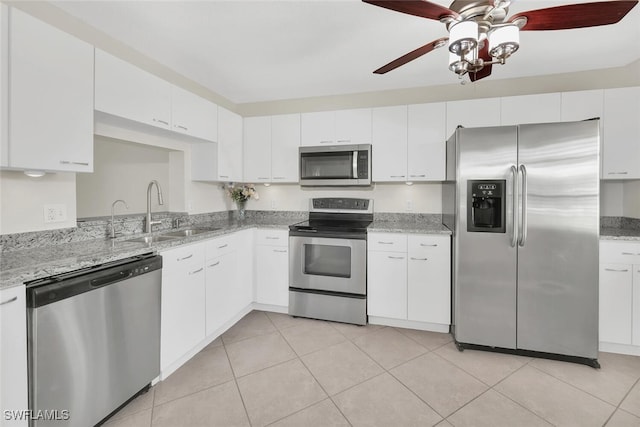 kitchen featuring light stone counters, light tile patterned floors, stainless steel appliances, white cabinetry, and a sink